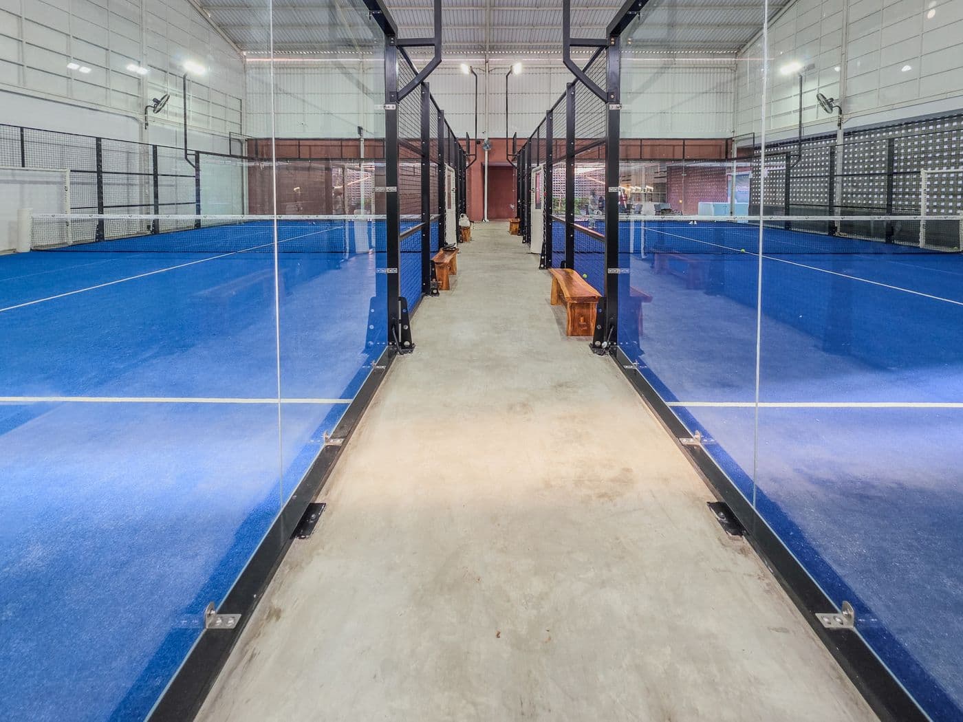 Multiple empty indoor Padel courts with blue surface and glass walls